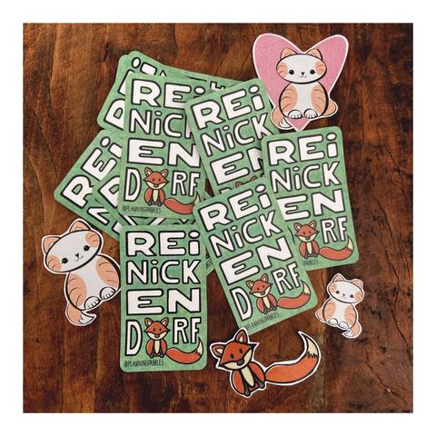 Meine selbst illustrierten Sticker, ausgeschnitten, durcheinander auf dunklem Holz liegend. 
Katze, Katze vor rosafarbenem Herz, Fuchs. Grüne rechteckige Sticker mit abgerundeten Ecken, auf denen REINICKENDORF steht. Das O wird durch den Fuchs ersetzt.