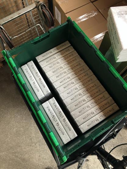 Photo d'un bac norme Europe vert contenant une série d'exemplaires de "Politiser l'enfance" sous blister. Le reste est entouré de cartons. On comprend que le bac est monté sur un vélo cargo Omnium.