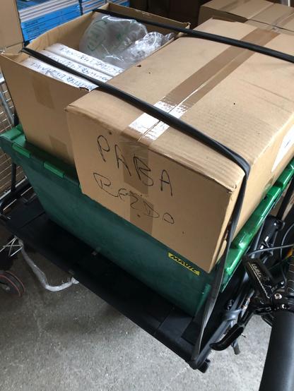Photo de cartons contenants des exemplaires de "Politiser l'enfance", posés sur un bac norme Europe vert conditionnés de sorte à être transportés sur le vélo cargo Omnium sur lequel ils ont été arnachés.