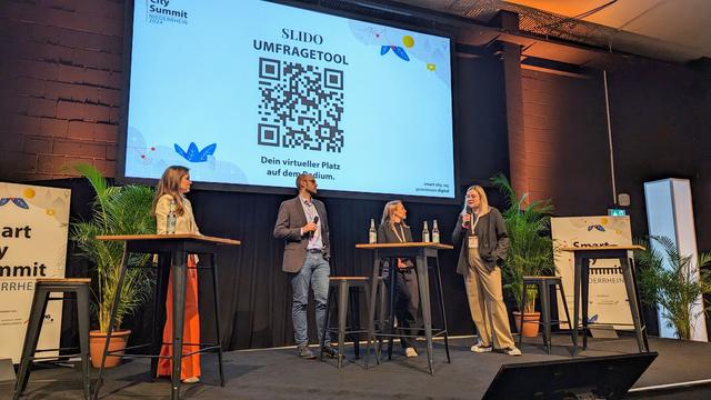Auf der Bühne sind drei Speaker:innen. Sie diskutieren zum Thema 
„Wie schaffen wir neue Wege der interkommunalen Zusammenarbeit?“
