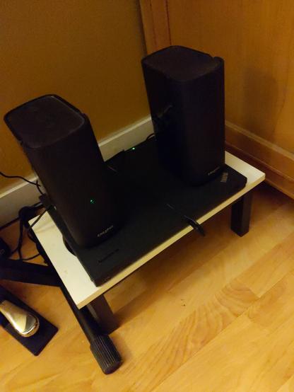 A closed thinkpad laptop with a pair of computer speakers sitting on top of it. They are sitting on a small wooden stand.