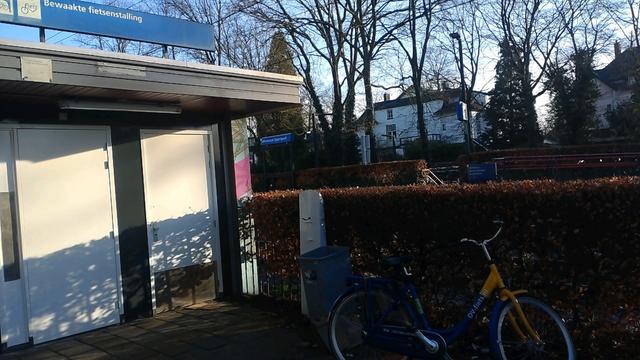 Bewaakte fietsenstalling met dichte deur en een paar losse ov-fietsen ernaast, op slot.