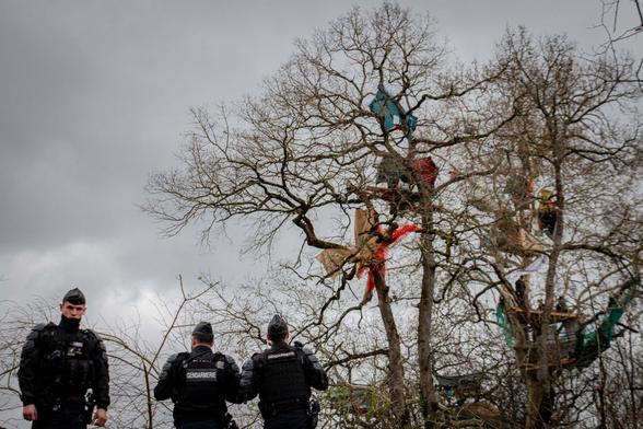 2 gendarmes francesos vigilen les persones que estan enfilades als arbres, entre una certa infraestructura muntada a les copes per quedar-s'hi força temps. Un tercer gendarme mira a la càmera amb cara de pocs amics