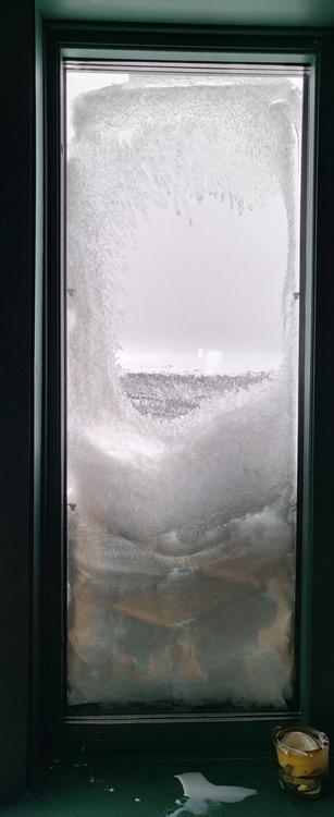 Ein Fenster, fast mit Schnee verdeckt. Gebirge im Hintergrund.