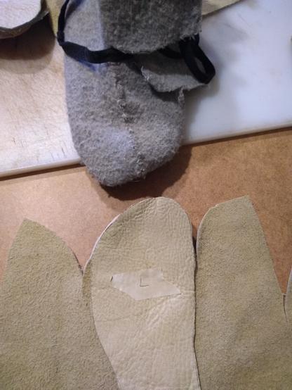 Closeup showing the leather for the left shoe laid flat. Toe to toe with the wool slipper of the same pattern showing how it folds up to form the center seam