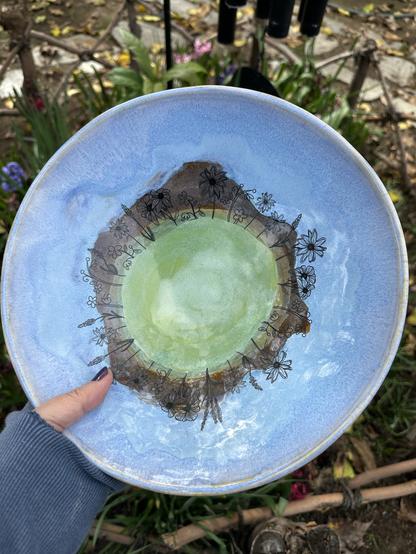 Wide shot of wildflower bowl. It’s blue with a strip of brown and green in the center. There is a circle of black wildflower in the middle