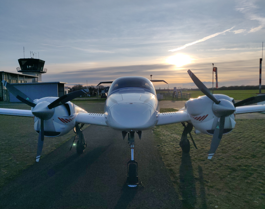 Frontalaufnahme einer Diamond DA42 kurz vor Sonnenuntergang im Gegenlicht