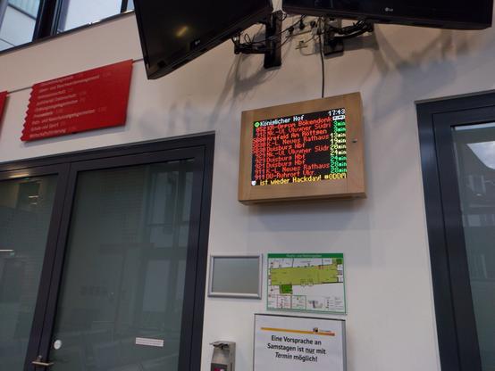 Led-matrix-Busabfahrtsanzeige im Rathaus Moers. 12 zeilen mit buntem Text. Unten läuft eine Scrollzeile mit ".. ist wieder Hackday!" und dem abgeschnittenen Hashtag