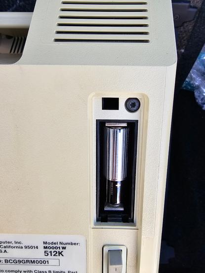 Battery compartment on the back of a Macintosh 512k with a vintage battery still in it.