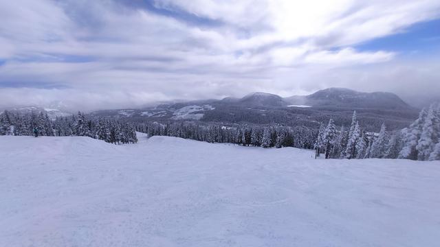 Panoramic view from Mount Washington. The mountain and the trees are covered in snow. The sky is blue with some clouds.