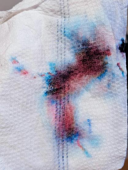 A white paper towel with a large splotch of maroon edged with fading pink and vibrant blues around the edges