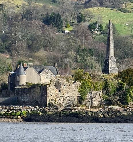 A ruined 14th century castle with a country house in the background and an obelisk on its right hand side.