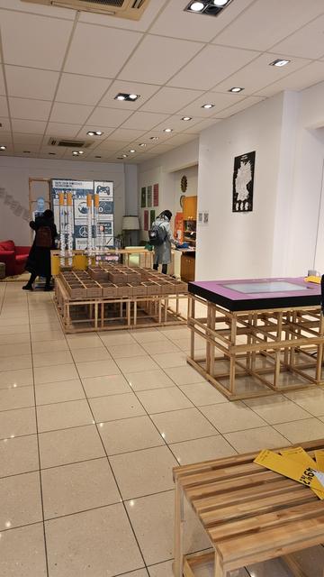 Blick in die Ausstellung. Auf der rechten Seite ein hölzerner Tisch mit einem eingelassenen Bildschirm. Geradeaus kleine Kartonschächtelchen, dahinter Übersichten und Röhren mit Tischtennisbällen, um die ungleich verteilten Chancen von Menschen in der deutschen Gesellschaft zu visualisieren.