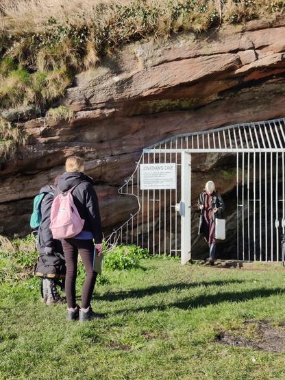 Cave entrance with metal grille. A woman stands in the opening and two women stand off to the left.