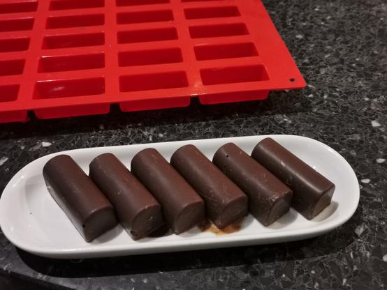 Zes zelfgemaakte bonbons met de siliconen mal op de achtergrond.