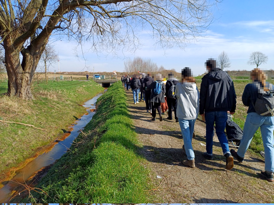 An einem braun-schlierigen Bachlauf mit knorrigem, kahlen Baum geht der Dorfspaziergang entlang. Im Hintergrund ein Polizeiwagen am Tagebaurand.