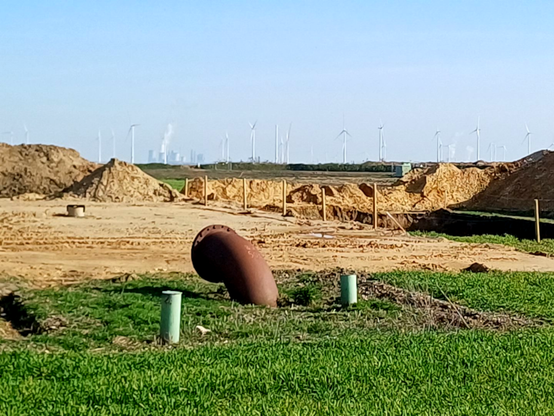 Baustelle mit Pumpen-Rohr für Grundwasser, im Hintergrund der Tagebau Garzweiler II mit Windrädern und Braunkohle-Kraftwerk