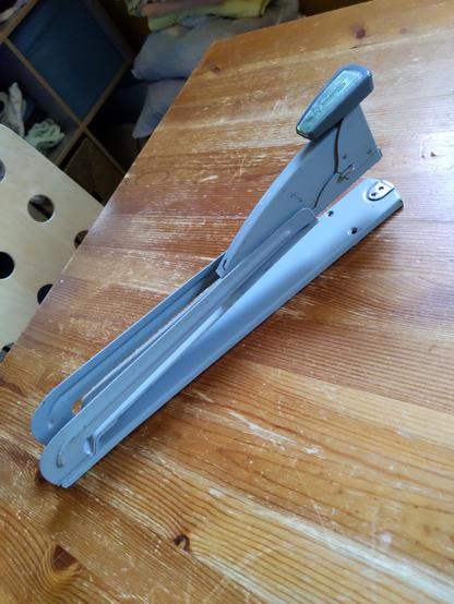 A gray booklet binding stapler sitting on a wooden table. It is the epitome of the phrase "old school".