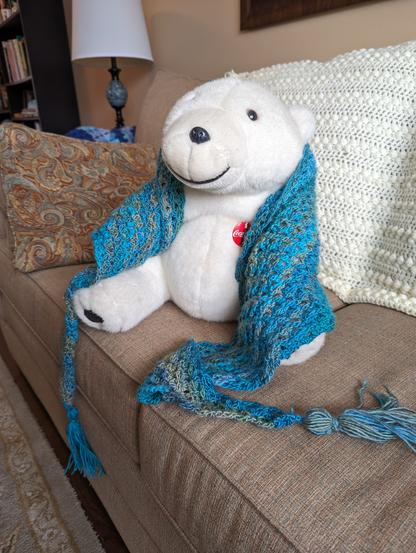 Large plush "Coca-Cola" polar bear wearing a mostly turquoise, variegated shawl with tassels at the corners.