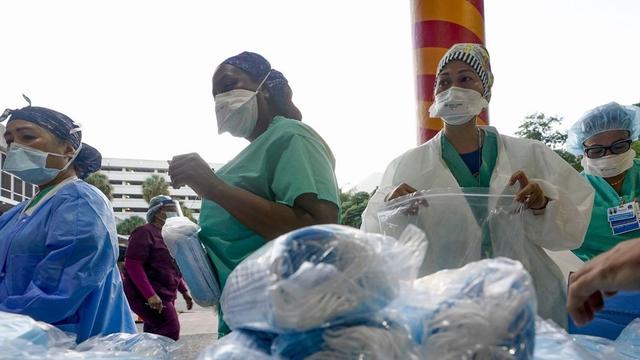 photo of several healthcare workers in masks, standing in front of a table of bags of scrubs and other garb