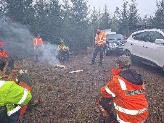 Skogshuggare som sitter runt en väldigt rökig eld i skogen. Två är instruktörer, de andra fyra är elever.