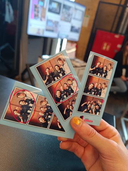A hand holding three photos with photos from a photo booth at a conference.