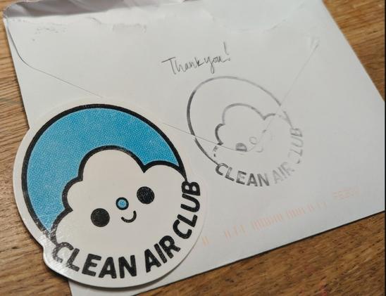 Photo of a sticker with a cute cloud and the words "clean air club", sitting on an opened envelope.