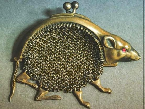 Rat legs dangle from the bottom of a round, chain mail mesh. The top of the purse is a solid piece shaped as the arched back of a rat, with the head to one side and the tail at the other. The red jewel in the eye makes it look creepy as fuck. Probably a French design by Paul Frey, or taken from such a design.