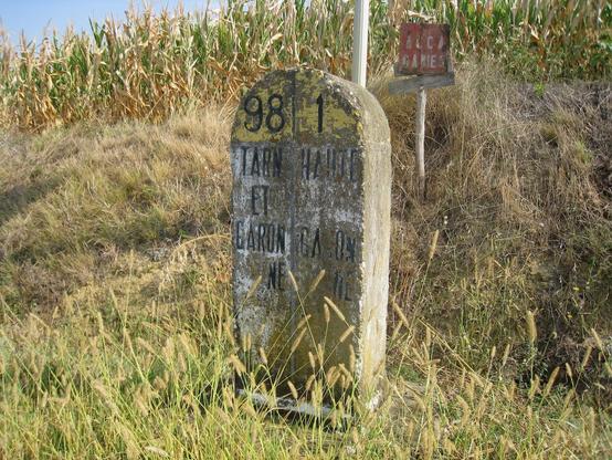 Devant un champs de maïs, une ancienne borne marque la délimitation des territoires départementaux de la Haute-Garonne et du Tarn-et-Garonne