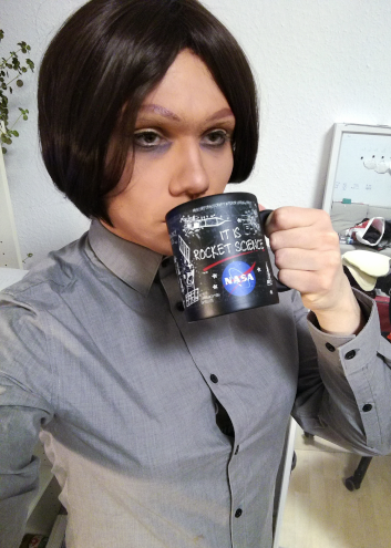 A cosplay selfie of the character Reagan Ridley from show Inside Job. She is looking exhausted and drinking from a mug labelled "IT IS ROCKET SCIENCE!"