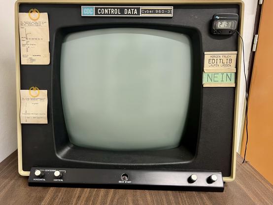 Vintage Control Data Corporation (CDC) computer monitor model Cyber 960-3 with paper tags and notes attached to it, and an electronic clock displaying on the top right side.