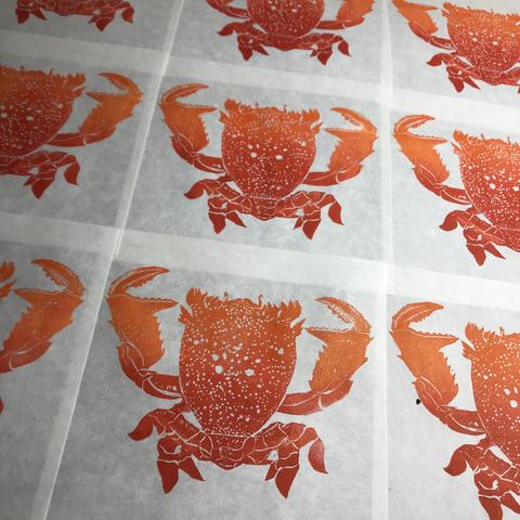 A collection of linocut prints laid out to dry of red and orange frog crabs (Ranina ranina) viewed from above.