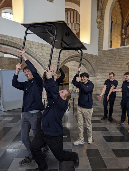 Four ULYSSIS members left up a table by the legs while two other members look on in surprise