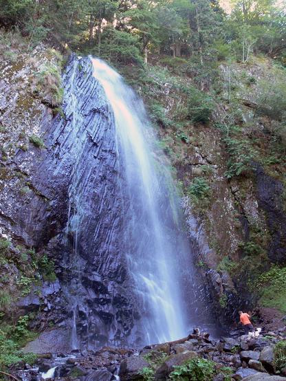 Vertical photo of a waterfall, falling over rocks in a forest.