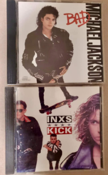 Two CD cases are laid next to each other. A copy of Michael Jackson's Bad, with Michael Jackson's head and torso, is above INXS's Kick album, which features a pair of legs on a skateboard toward the top of the album art. Together, it looks like a massive Michael Jackson with tiny legs is riding a skateboard.