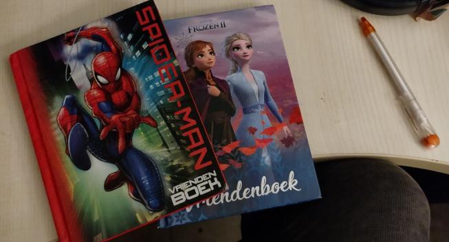 Een bureau met een pen en twee vriendenboekjes erop. Een van spiderman en een van Frozen.