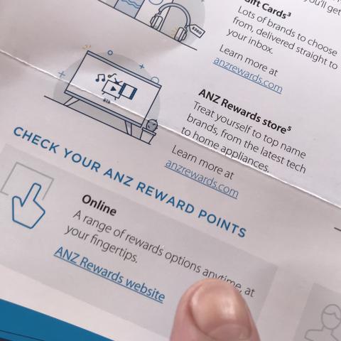 Printed brochure from ANZ, including some blue-underlined text that is probably meant to look like web hyperlinks. Several show a web address (anzrewards.com), but one only shows text (ANZ Rewards website).
A finger hovers hesitatingly over the latter, unsure whether to tap or not.