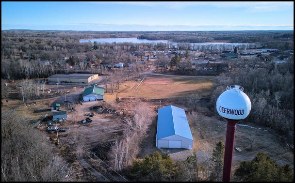 Aerial photograph of a small town water tower. Water tower says "Deerwood." Behind water tower we see a softball field and some houses.