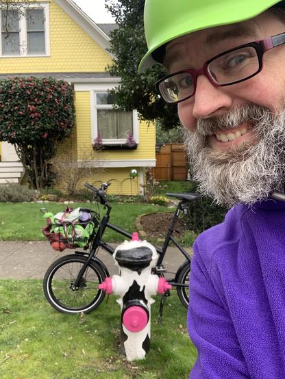 Smiling guy standing in front of a bike next to a hydrant painted like a cow.