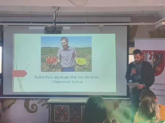 Plansza wyświetlona na ekranie rzutnika pt. Rolnictwo ekologiczne na Ukrainie. Obok stoi osoba prezentująca.