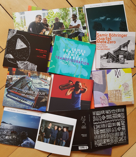 assembly of jazz CDs and CD booklets on wooden floor: top right to bottom left: James Brandon Lewis Quartet, Nitai Hershkovits, Wadada Leo Smith/Joe Morris, Samir Böhringer Quartet, Sophie Alour, Umlaut Chamber Orchestra, John Surman, Abdullah Ibrahim 3