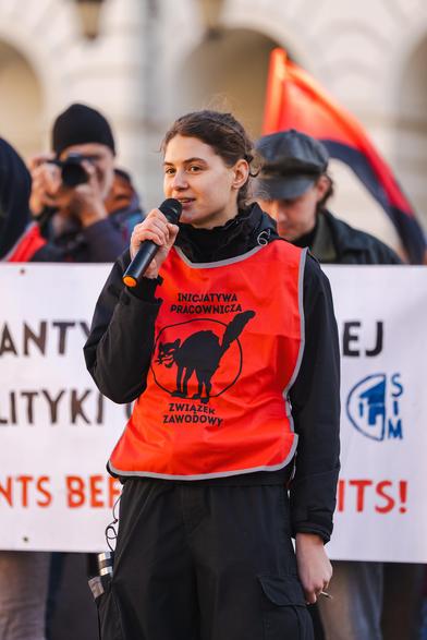 Młoda kobieta z mikrofonem w czerwonej kamizelce Inicjatywa Pracownicza