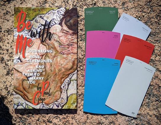 A copy of Be With Me along with some colorful paint swatches from the hardware store you might use to inspire the prospective life partners you date playing the game.