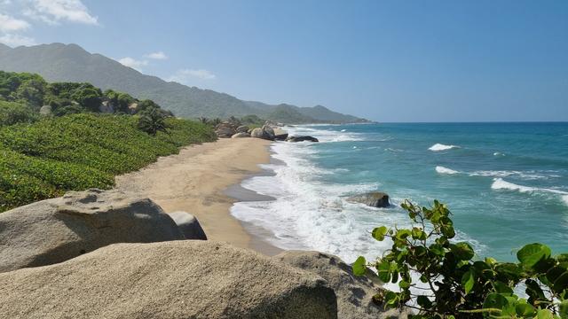 Jungly hills to the left roll into a sandy beach, which leads to a beautiful blue but angry sea to the right.