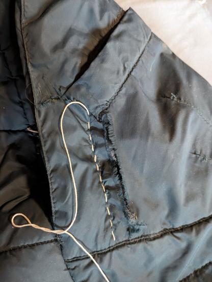 Eine Jackentasche auf einer grünen Jacke mit einem Riss. Eine einzelne naht mit weissem sashiko Faden ist genäht.