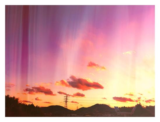 A wide shot of the countryside just before dusk. It consists of a row of small mountains with a power line running through it, mostly in shadow. The light is coming in from the right. The shot, as usual, is mostly sky with just a few clouds in it. And I've layered this image with a filter that gives it a reddish hue with vertical brush strokes running through it. I added a white frame around it as well.