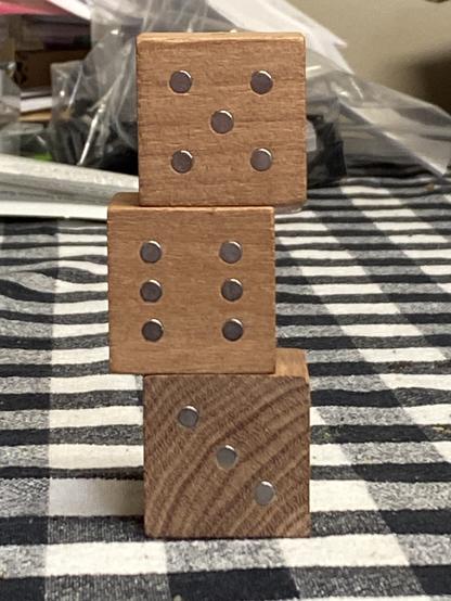 Three six-sided wooden dice stacked on top of each other on a striped cloth surface. The top die shows five dots, the middle four, and the bottom three.