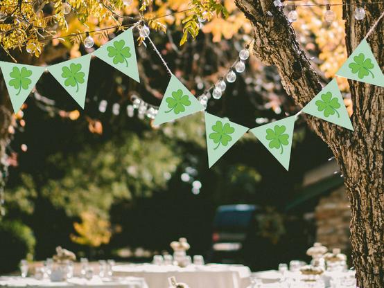 A pale green bunting banner with bright green shamrocks strung along a set of lights on an outdoor patio at a party