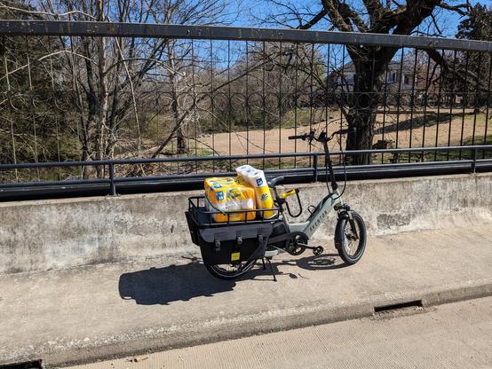 Electric cargo bike laden with large pack of paper towels, toilet paper, and saddle bags. Photo on a bridge