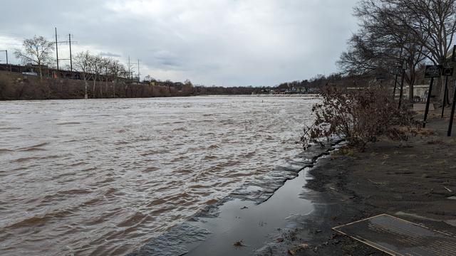 Choppy water almost up to the level of the walkway with trees in the background